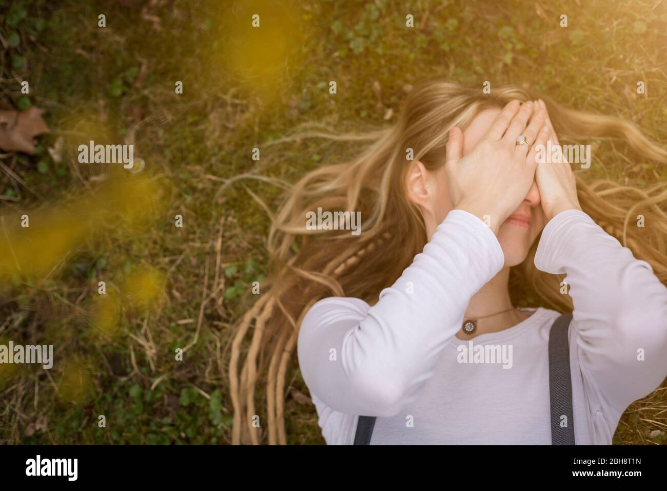 Close-up portrait of a happy young blond woman holding dreadlocks kneeling holding a yellow blossom in a spring garden Stock Photo