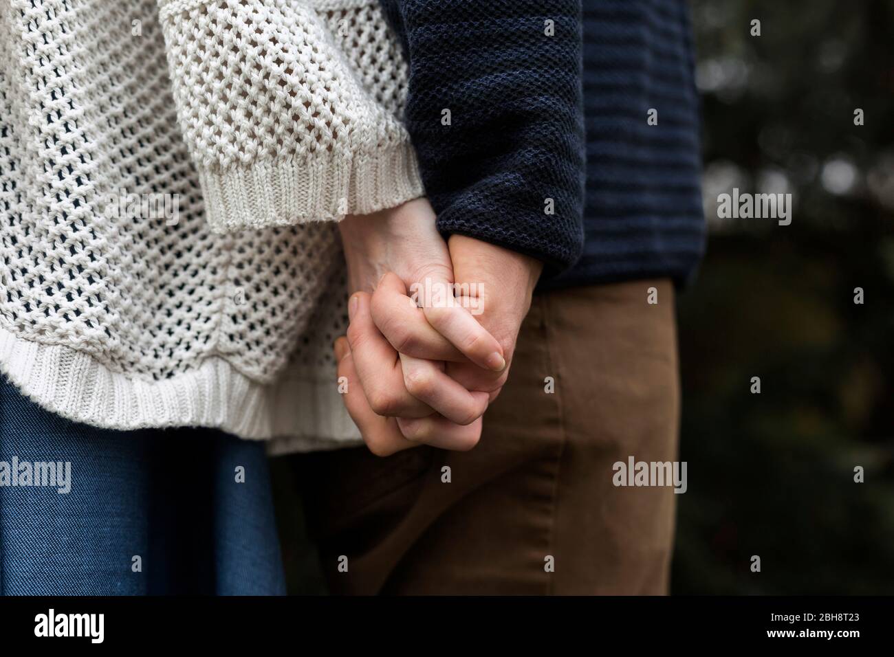 Young couple in love clasping hands as they stand back to back outdoors in their hands Stock Photo