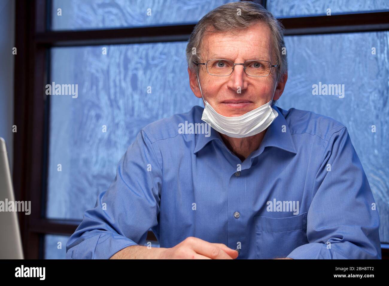 Portrait of a friendly smiling doctor at his desk wearing a surgical mask - focus on the face Stock Photo