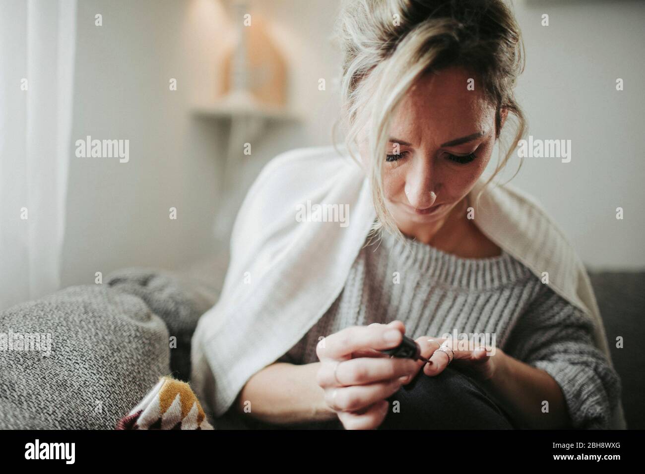 Frau sitzt entspannt auf der Couch, lackiert sich die Fingernägel Stock Photo