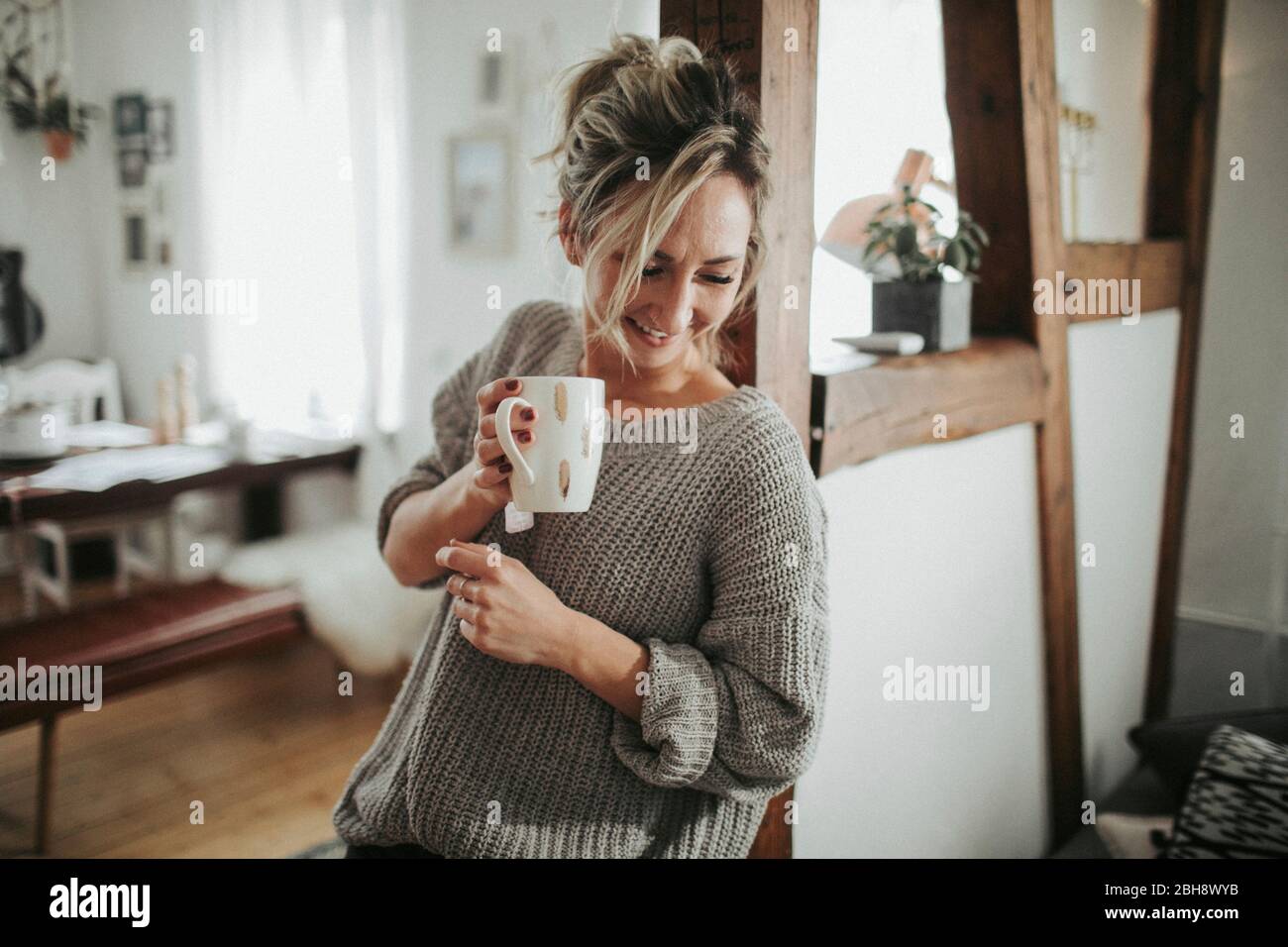 junge Frau in ihrer Wohnung, hält Tasse in der Hand, lachen, Halbporträt Stock Photo