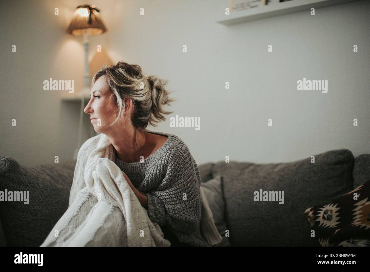 Frau sitzt nachdenklich auf der Couch Stock Photo