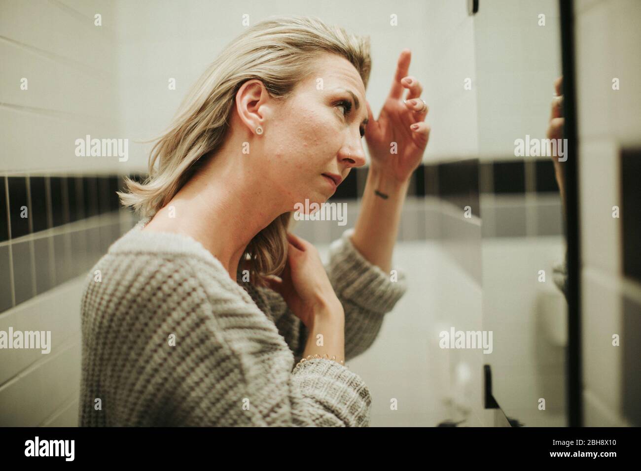 Frau im Badezimmer, betrachtet kritisch ihr Spiegelbild Stock Photo