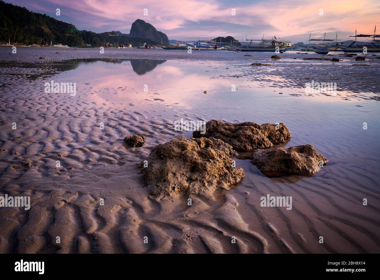 Blue hour at tropical harbor bay in evening. Tranquil sunset in lagoon shallow water and sandy beach in Philippines, Palawan, El Nido. Sundown on beach. Scenic view with mountains isles on horizon. Stock Photo