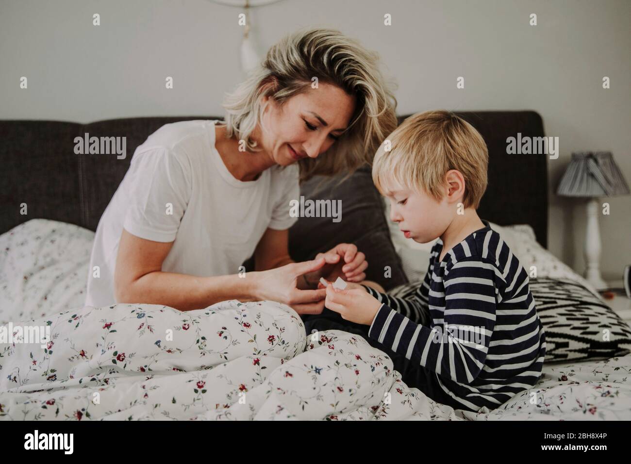 Morgens im Bett, Mutter verarztet Wunde am Finger ihres Sohnes Stock Photo