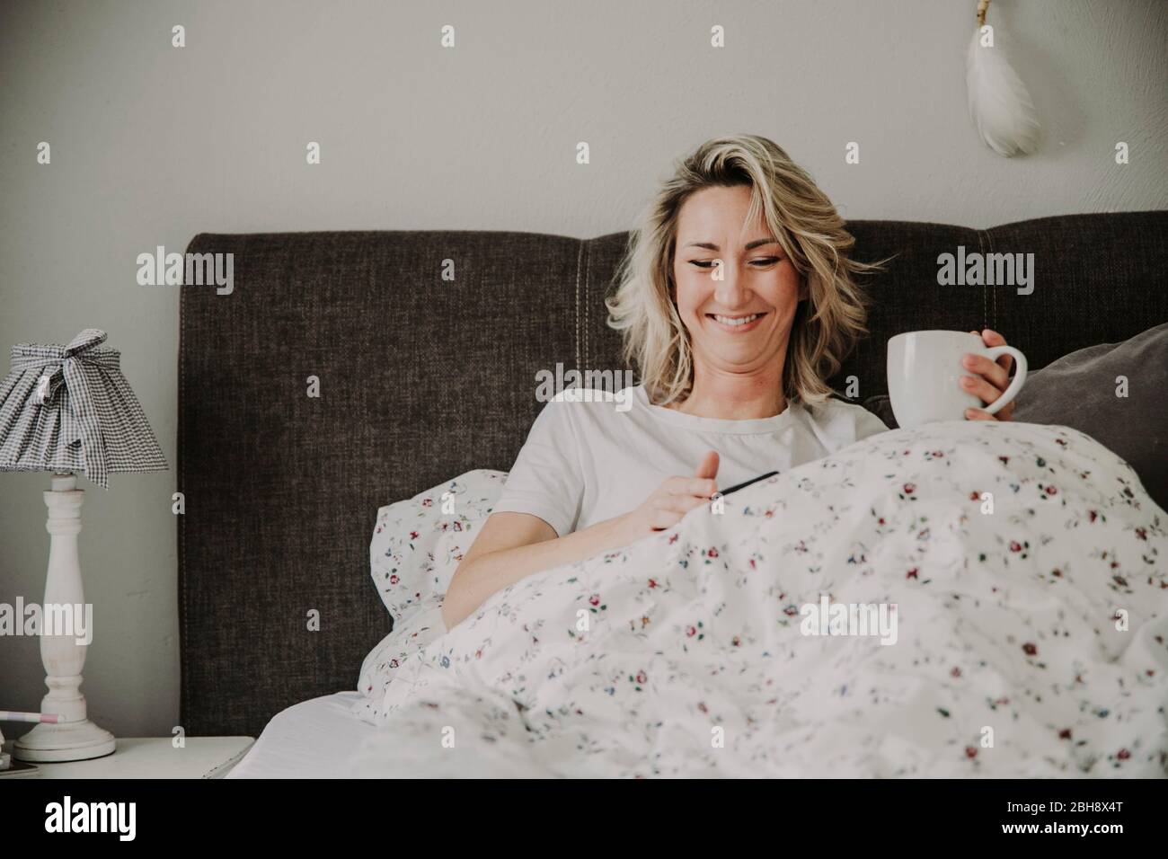 Frau mit Kaffeetasse und Smartphone im Bett Stock Photo