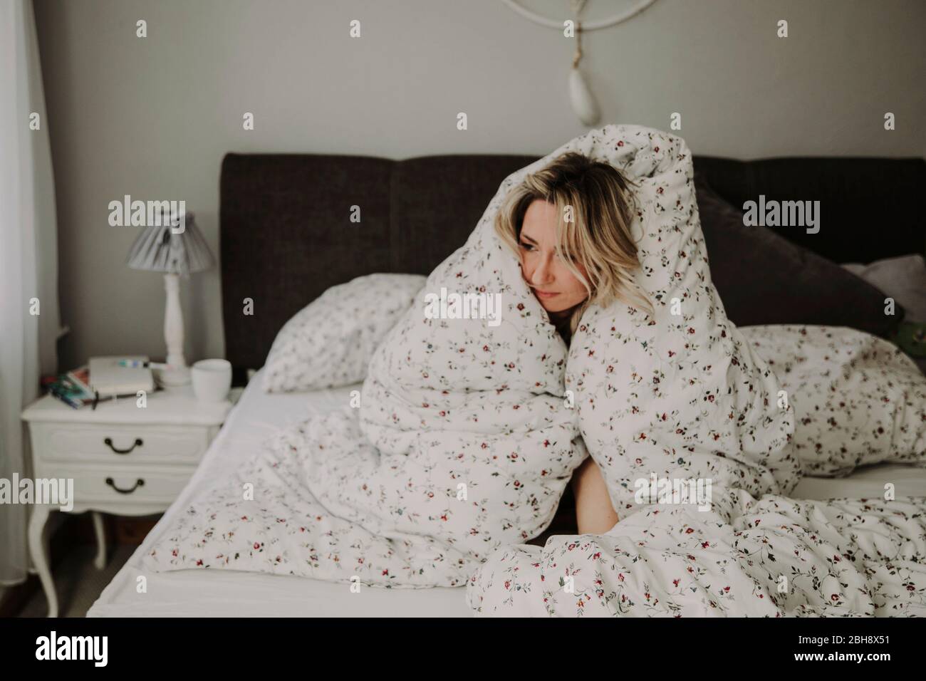 Frau in Bettdecke eingehüllt im Bett, müde, antriebslos, Nahaufnahme Stock Photo
