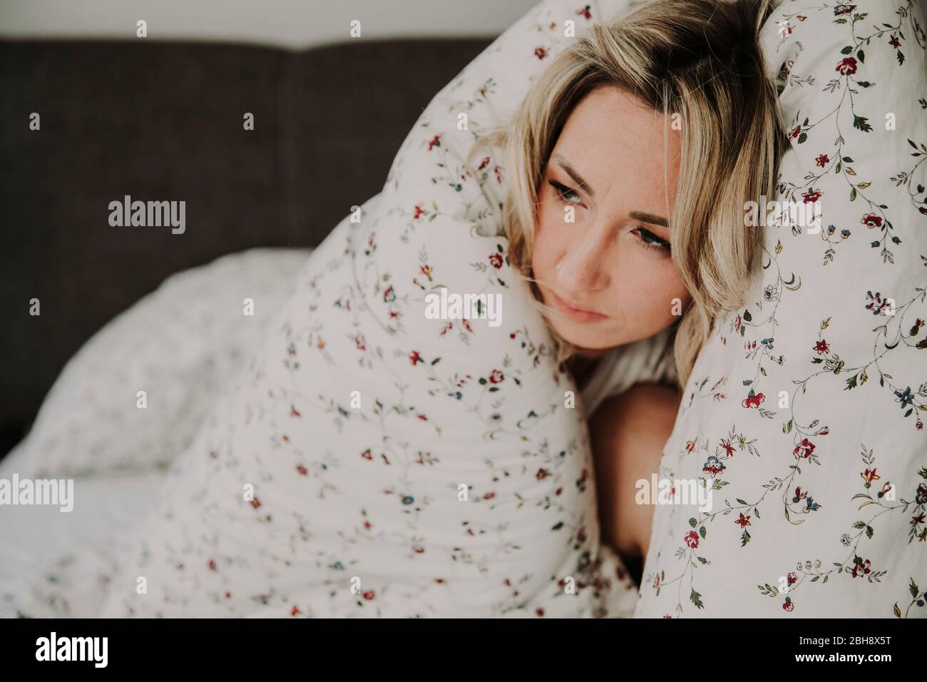 Frau in Bettdecke eingehüllt im Bett, müde, antriebslos, Nahaufnahme Stock Photo