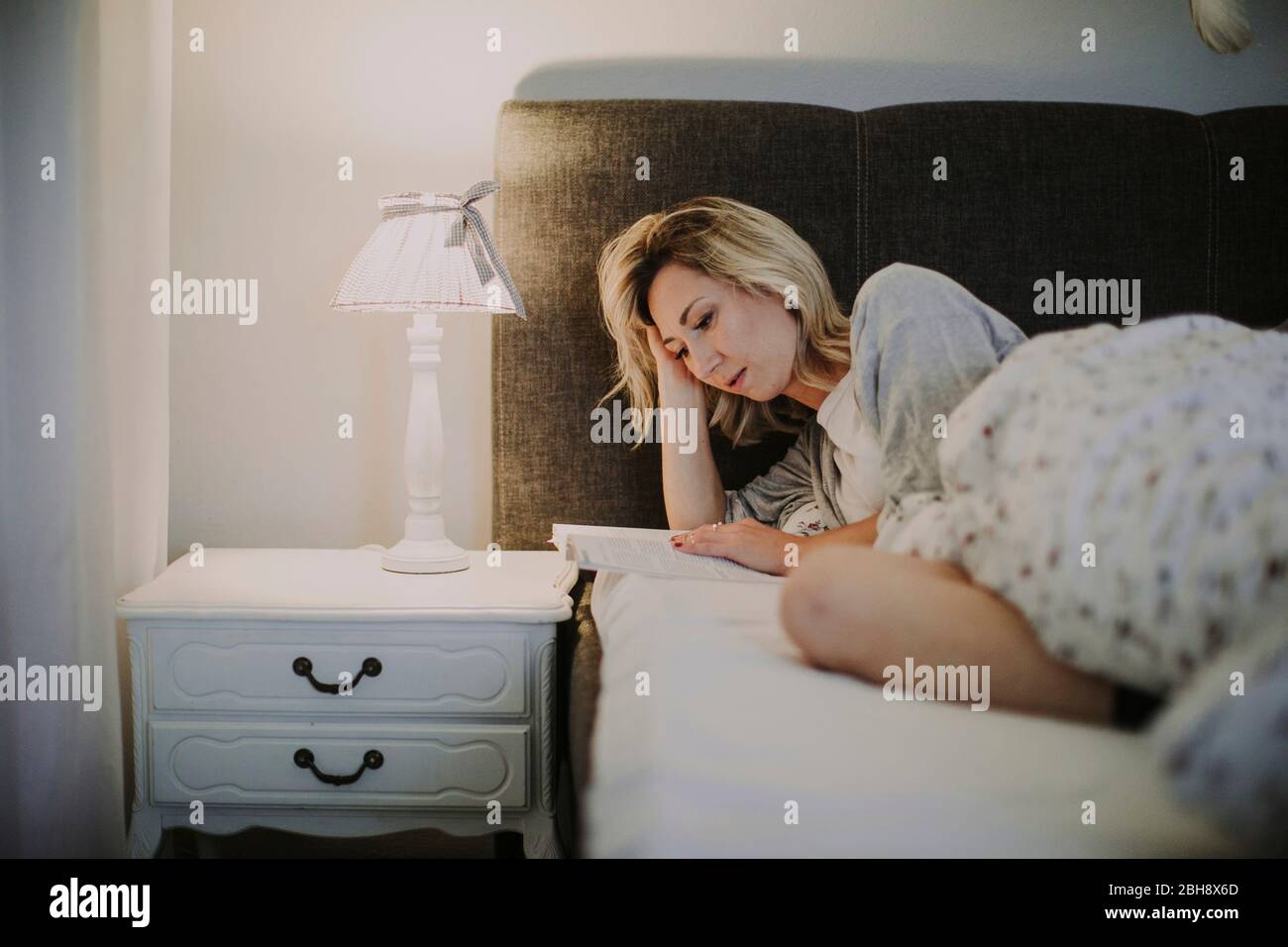 Frau liegt mit Buch im Bett Stock Photo