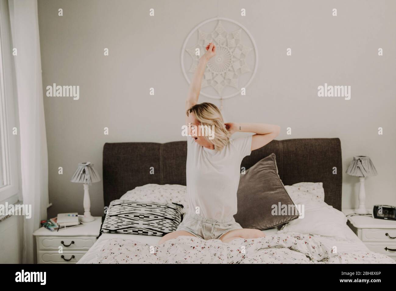 Woman sits in bed yawning and stretches Stock Photo