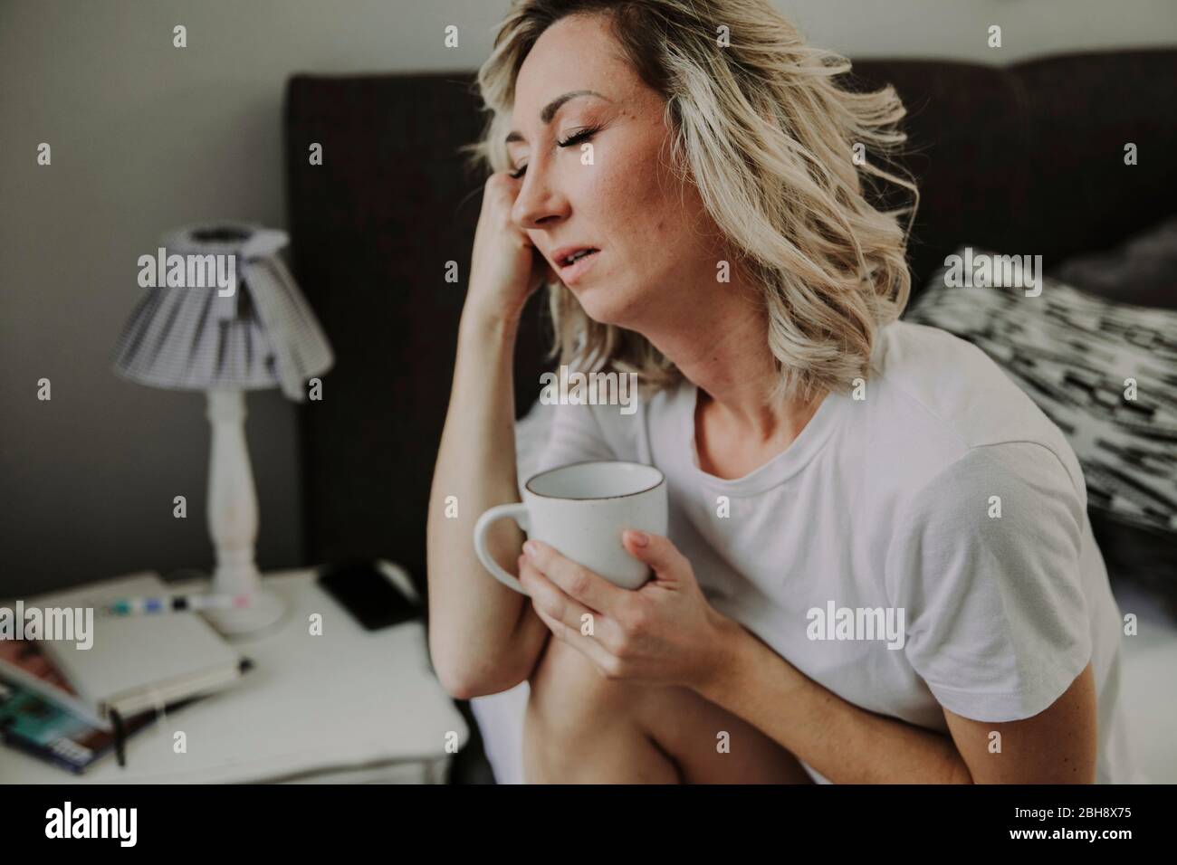 Frau mit Kaffeetasse im Bett, müde, unausgeschlafen Stock Photo