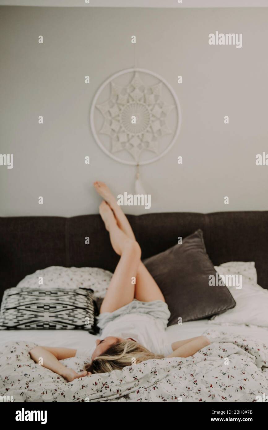 Frau liegt entspannt im Bett, Beine hochlegen Stock Photo