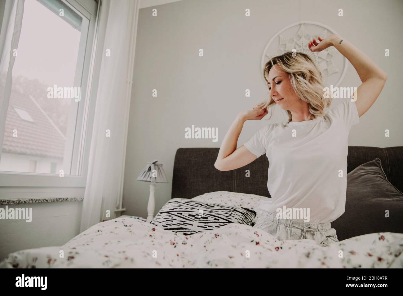 Woman sits in bed and stretches Stock Photo