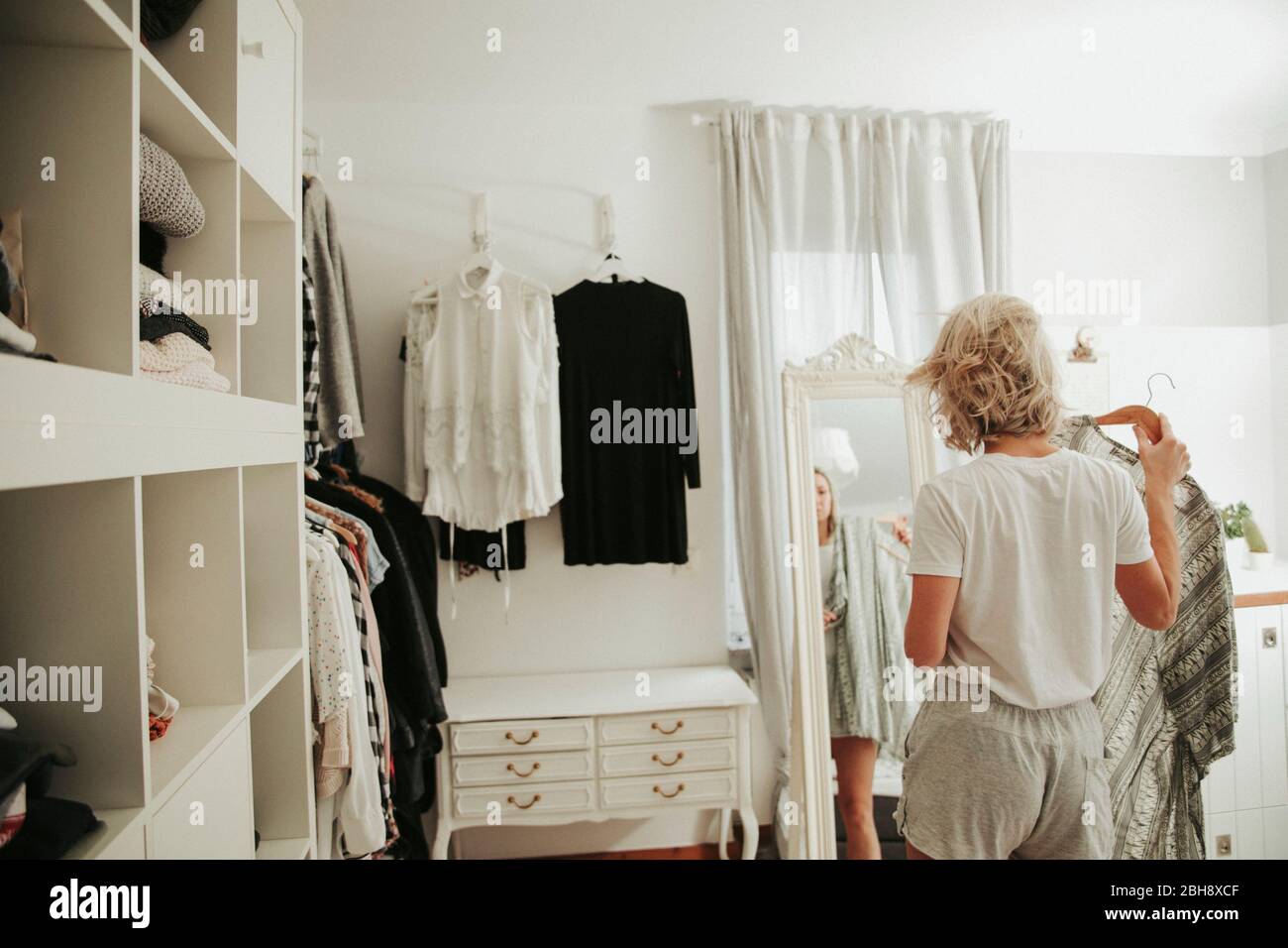 Frau steht vor dem Spiegel, kleidet sich an, unentschlossen Stock Photo