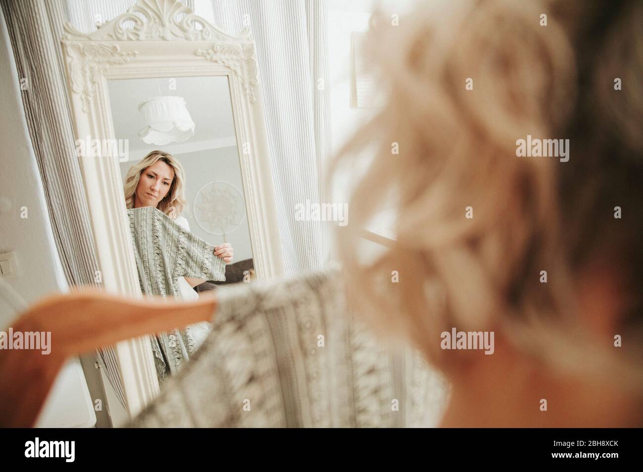 Frau steht vor dem Spiegel, kleidet sich an, unentschlossen Stock Photo