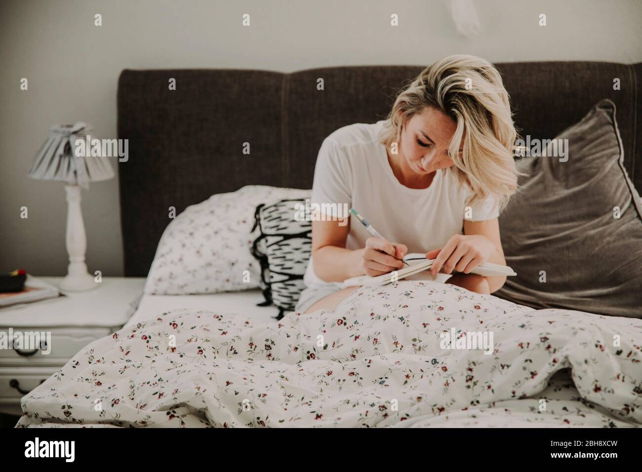 Frau sitzt mit Notizbuch nachdenklich im Bett Stock Photo