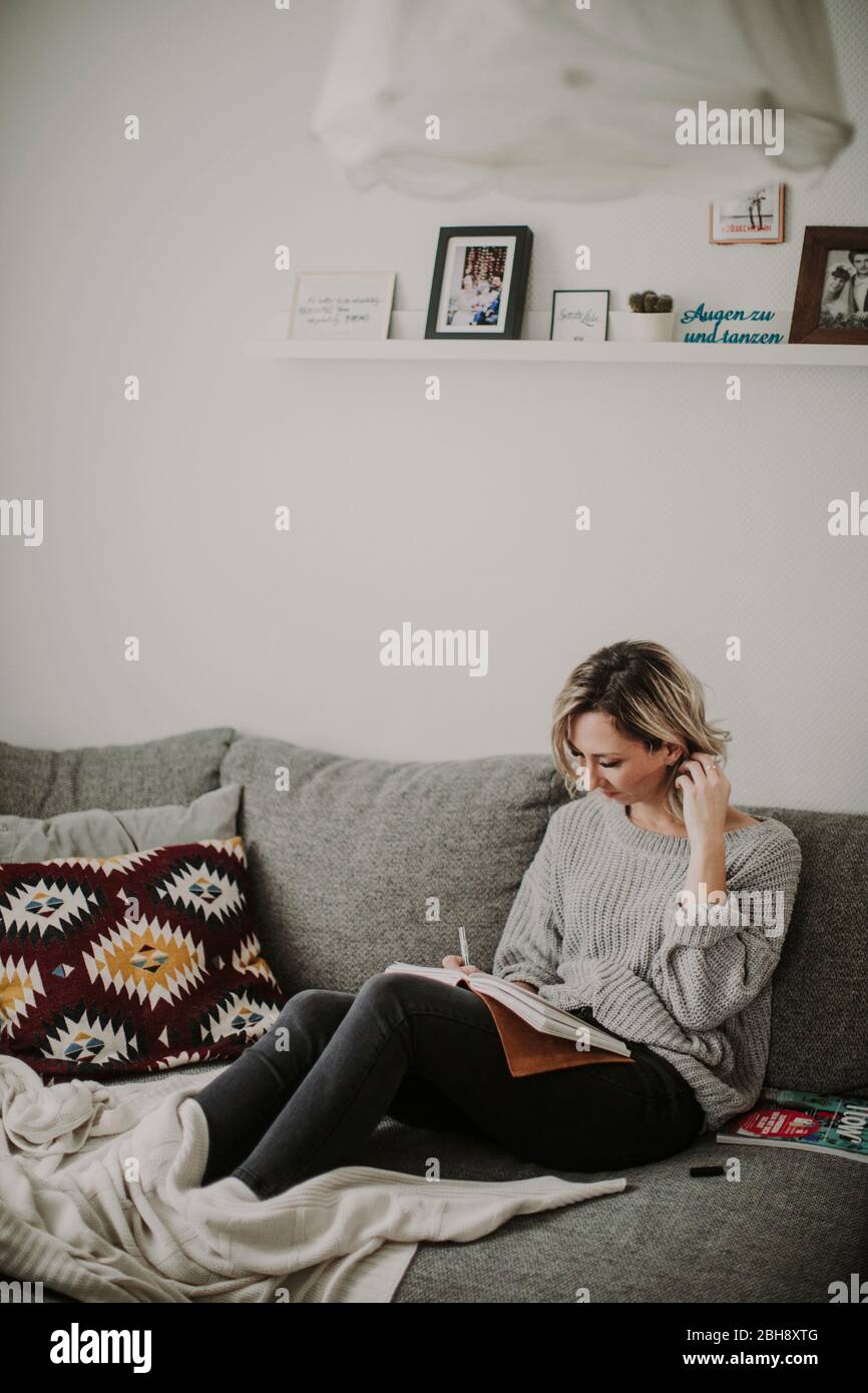 Frau mit Notizbuch und Zeitschrift auf der Couch Stock Photo