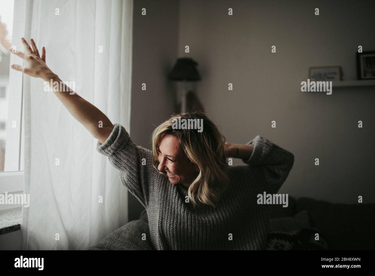 Frau blickt freudig aus dem Fenster Stock Photo