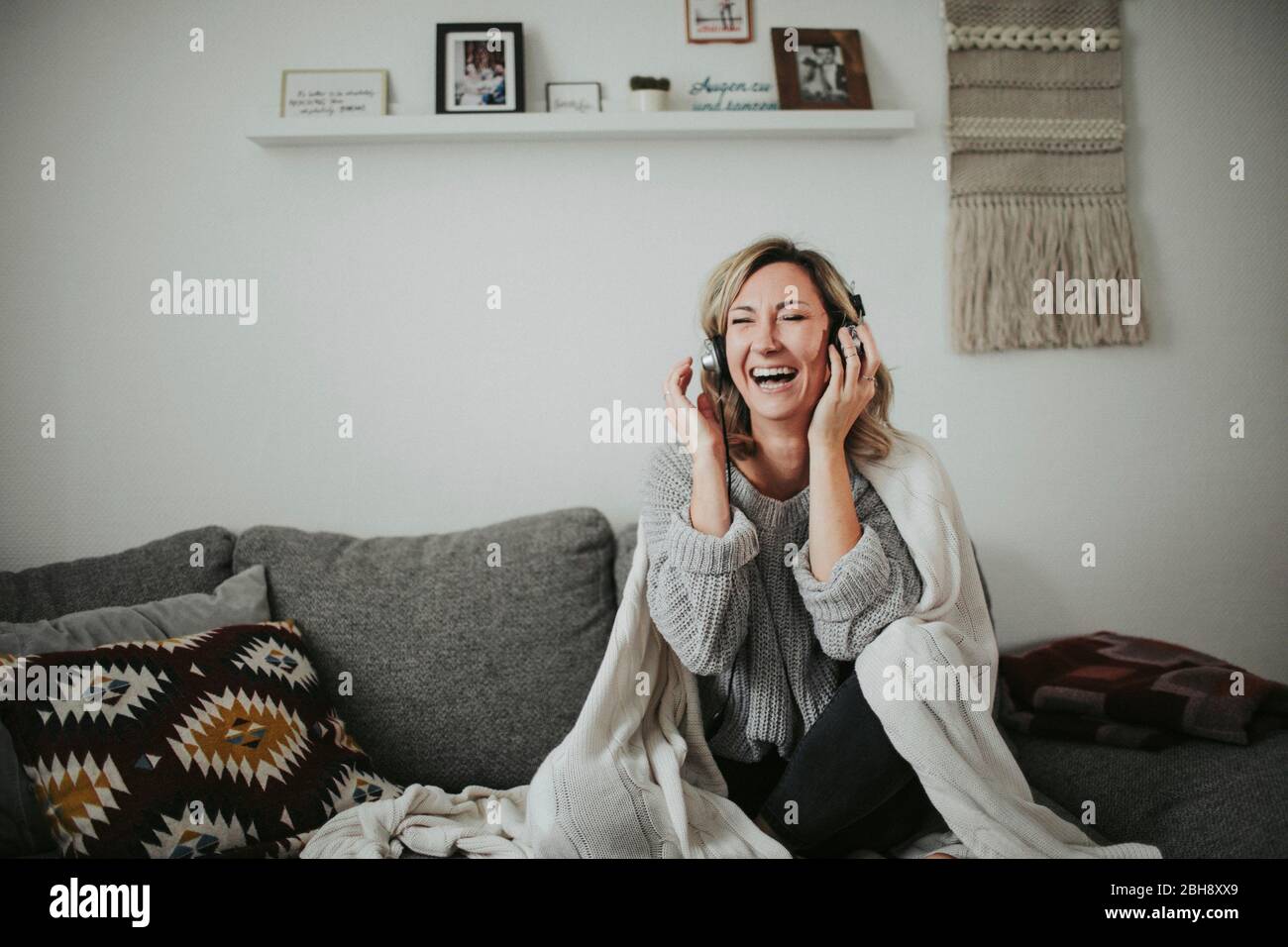Frau sitzt fröhlich auf der Couch, Musik hören, Kopfhörer, lachen Stock Photo