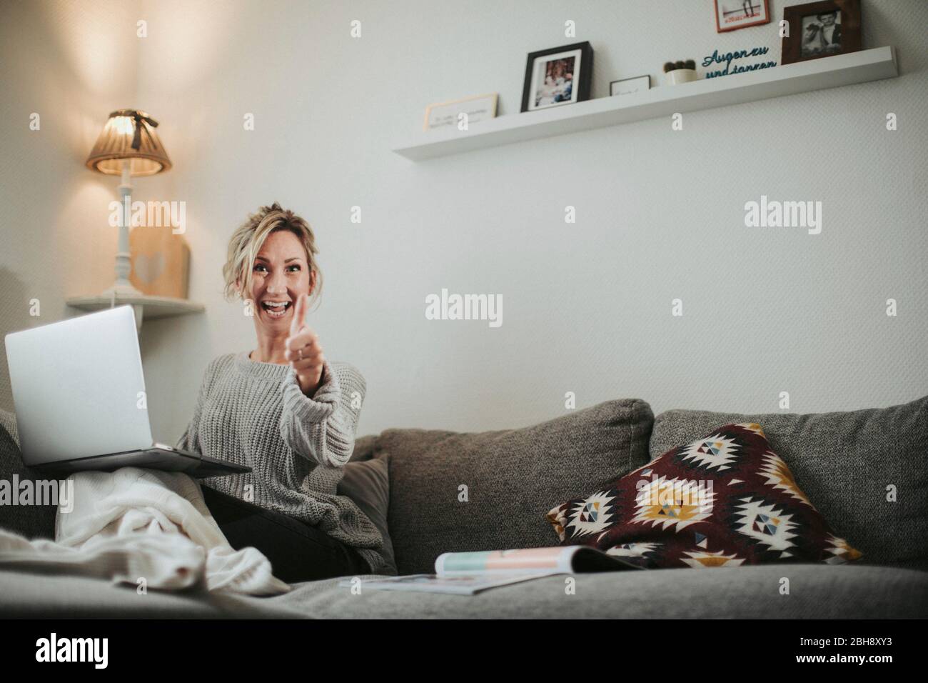 Frau sitzt entspannt mit Laptop auf der Couch, Freude, Daumen hoch Stock Photo
