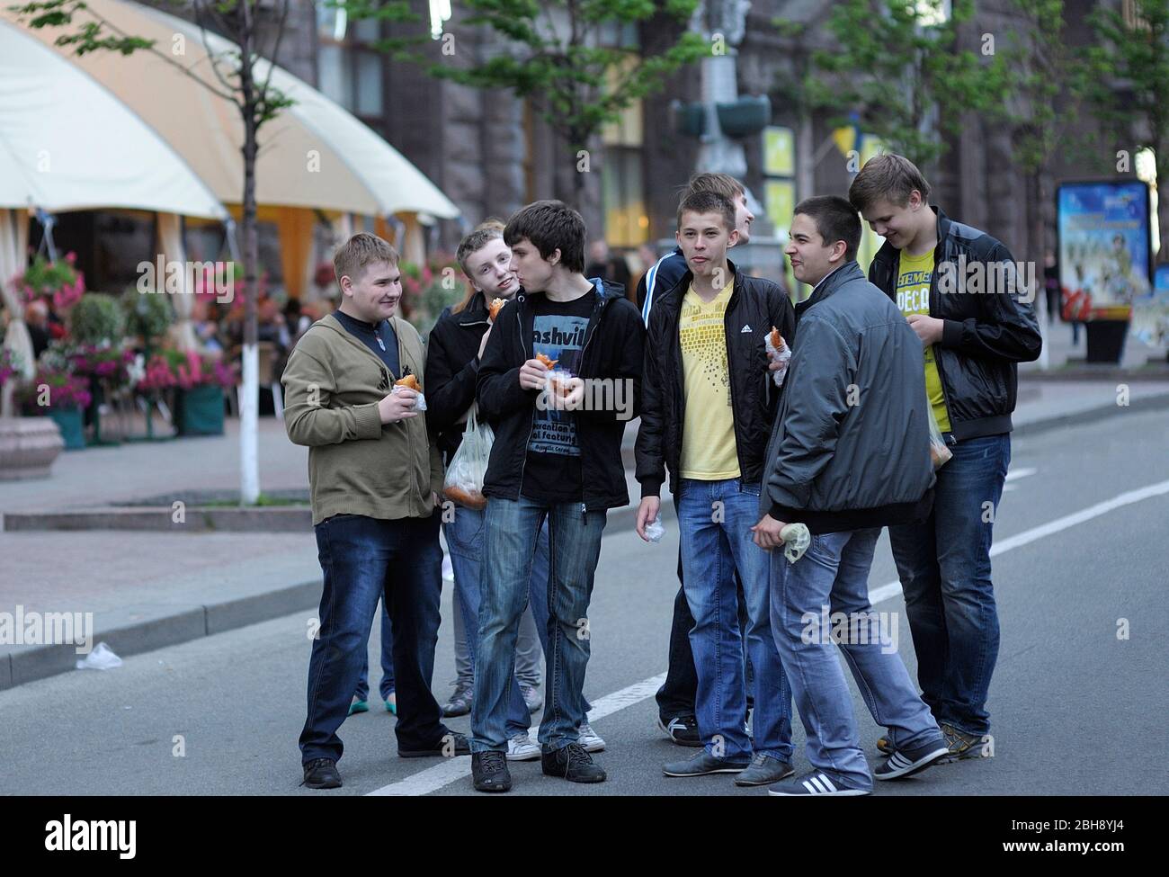 Group of laughing young boys standing in the street and eating burgers Stock Photo