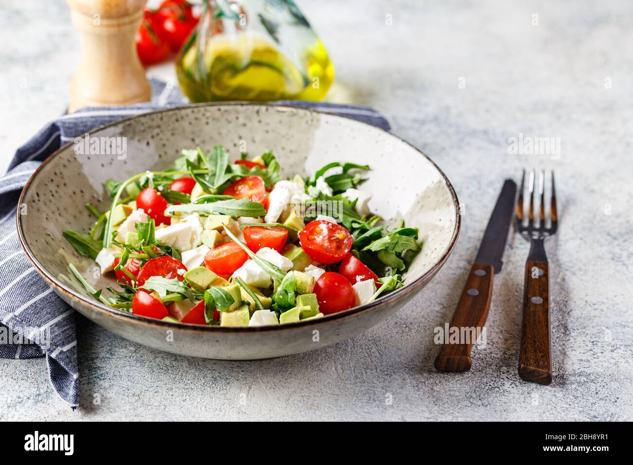 Green salad with avocado, cherry tomatoes and feta cheese. Healthy diet vegetarian summer vegetable salad. Table setting, food concept. Stock Photo