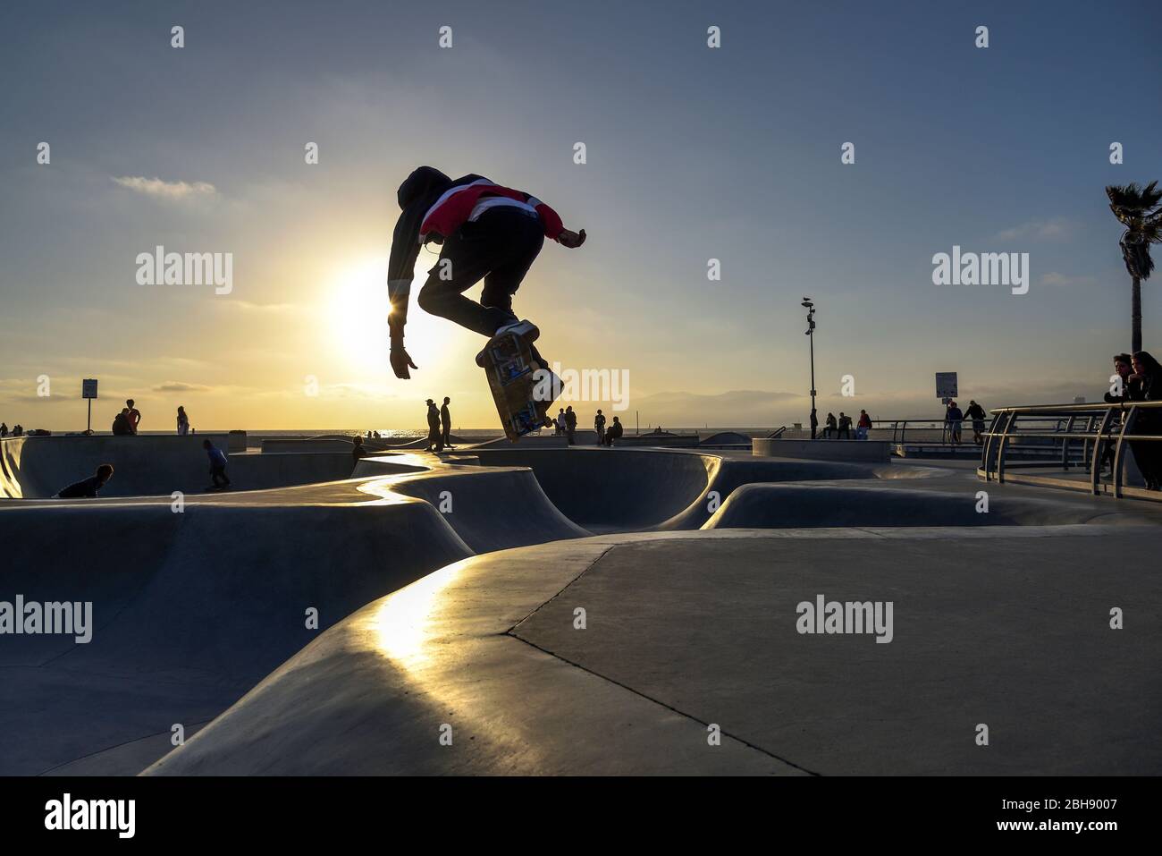 Skater mit seinem Skateboard beim Springen im Skate Park in Los Angeles, Sonnenuntergang, Zuschauer am Rand der Skate Bahn Stock Photo