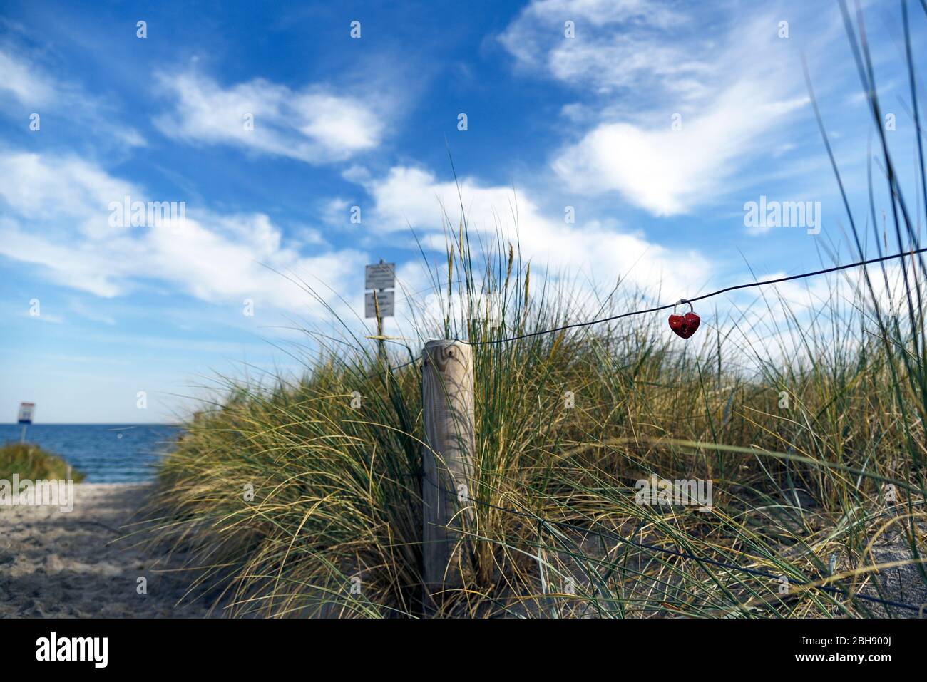 Blick durch das Dünengras an einem Strandzugang in Ahrenshoop auf die Ostsee und ein rotes Vorhängeschloss in Herzform Stock Photo