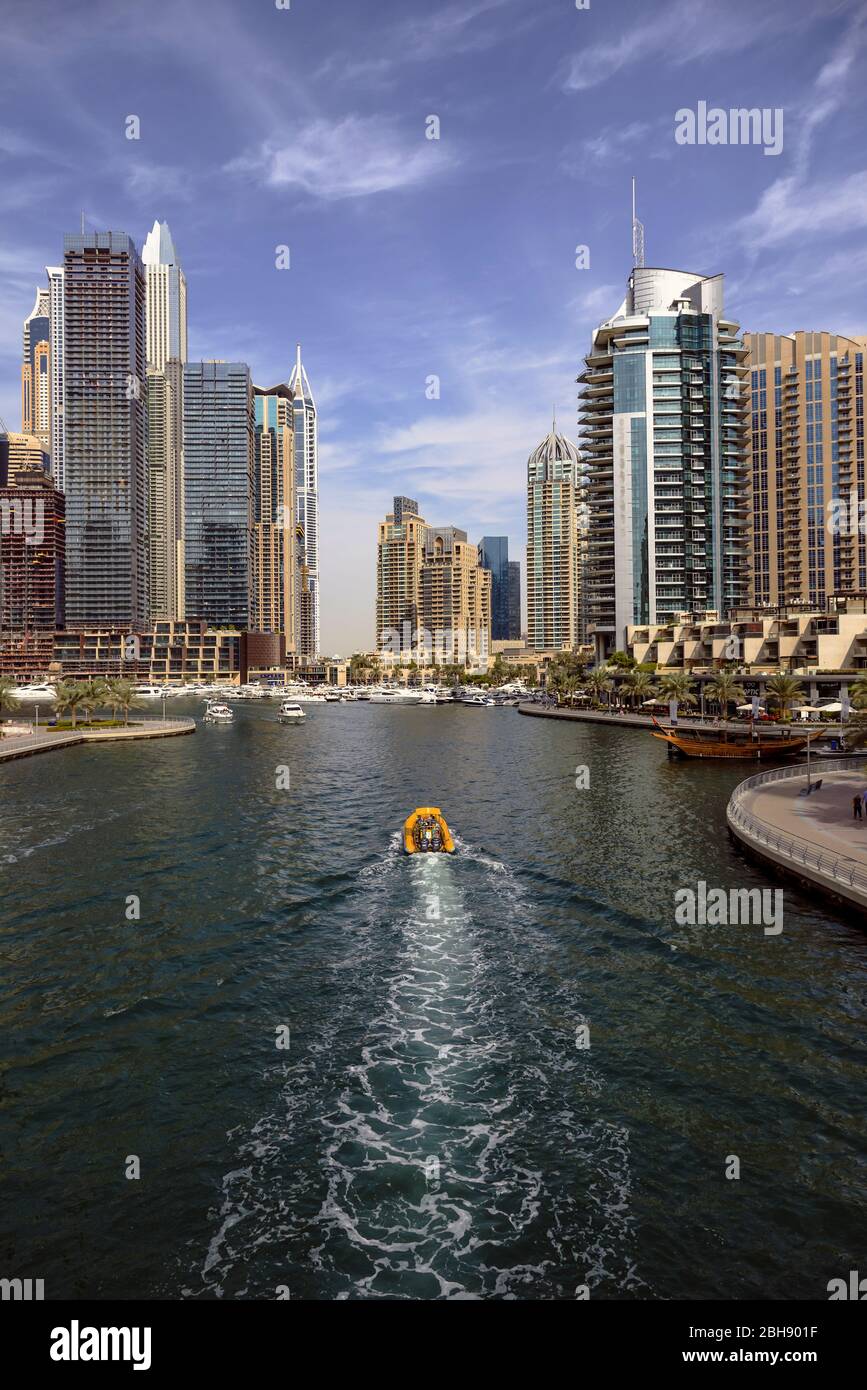 Blick auf ein Boot das gerade in den Hafen von Dubai Marina fährt, Uferpromenade und moderne Wolkenkratzer Stock Photo