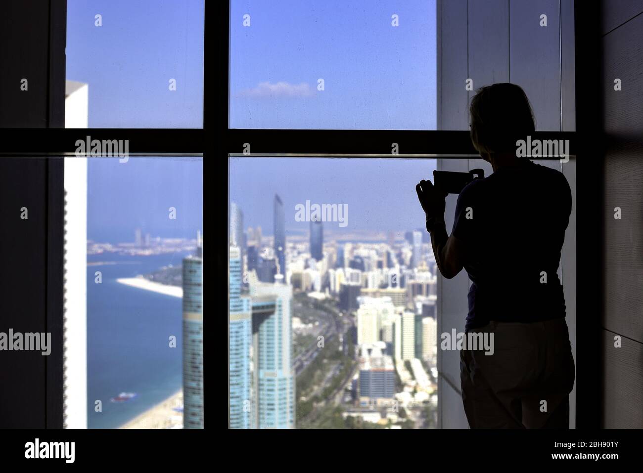 Touristin am Fenster, fotografiert die Aussicht auf Abu Dhabi mit dem Smartphone, Silhouette Stock Photo