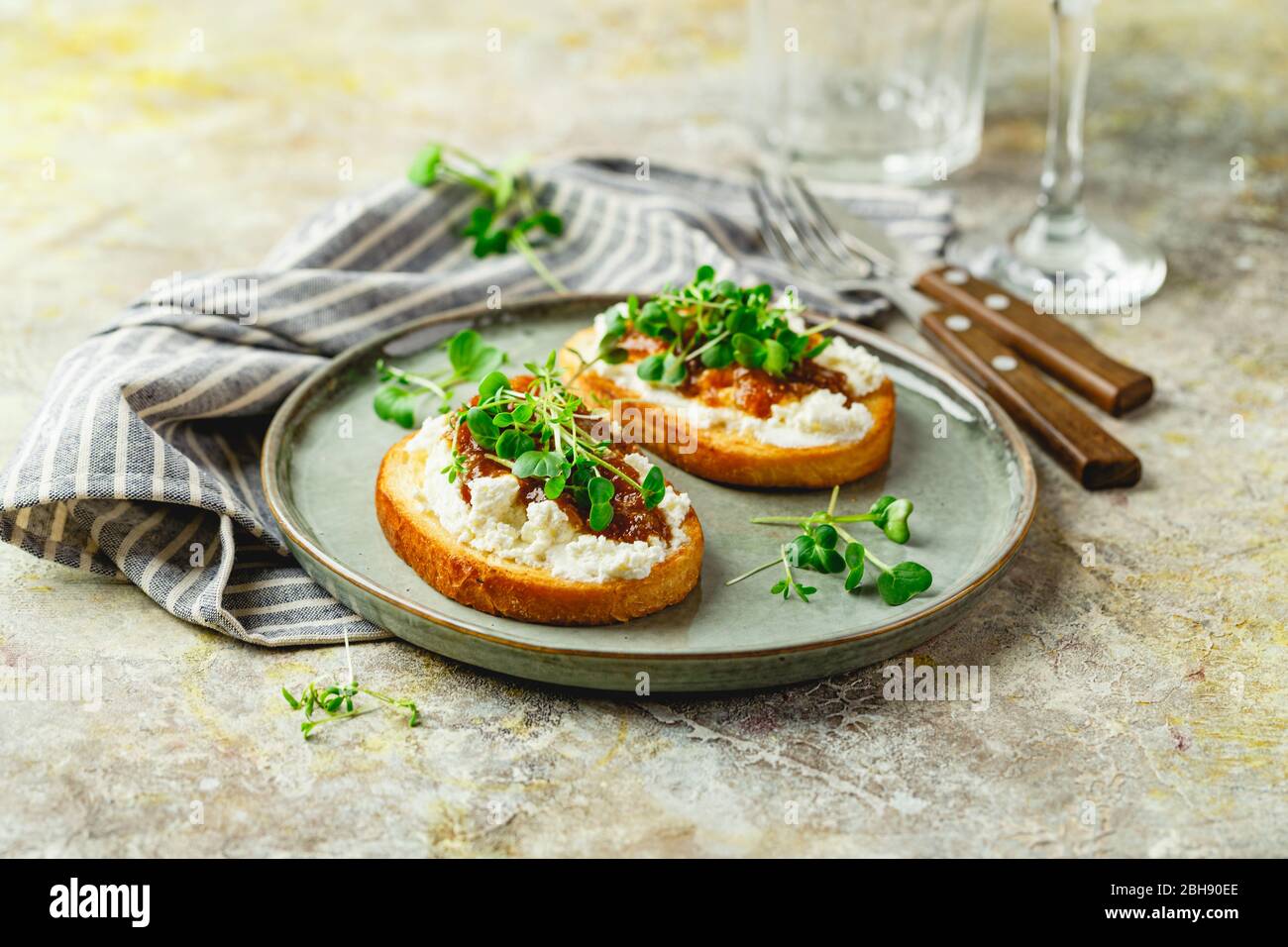 Canape or crostini with toasted baguette, cottage cheese, fig jam and microgreen on plate. Delicious breakfast, snack, appetizers Stock Photo