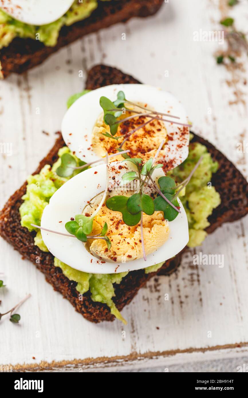 Healthy toast on rye bread with avocado, boiled eggs, spices and microgreen on white wooden