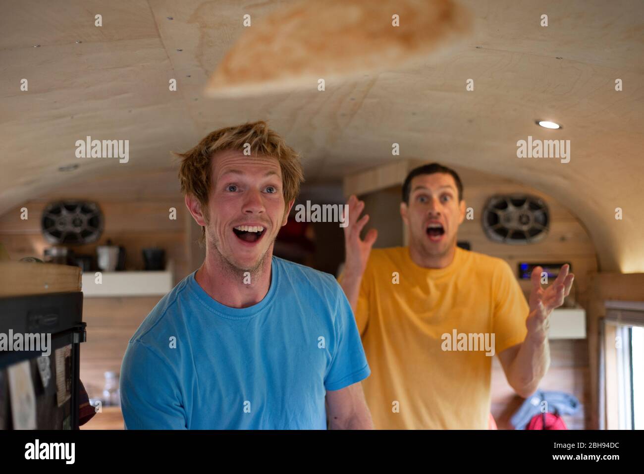 Two people making funny face while flipping crepes inside school bus Stock Photo