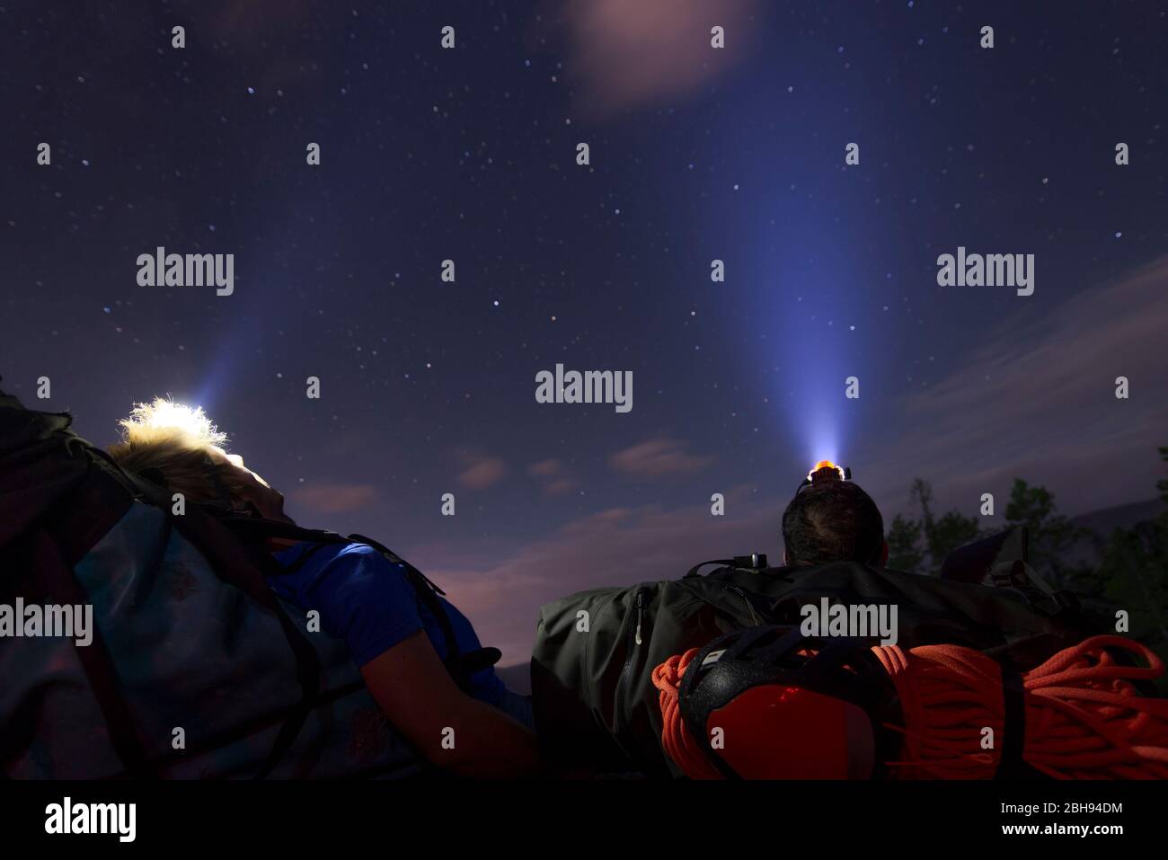 two people laying down on backpack under the stars with headlamps Stock Photo