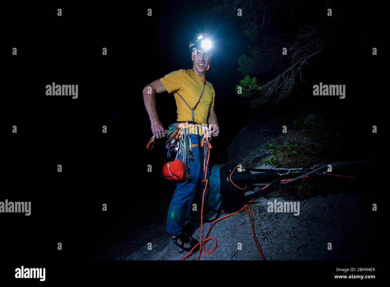 Man finishing rock climbing at night with headlamp top of climb Stock Photo