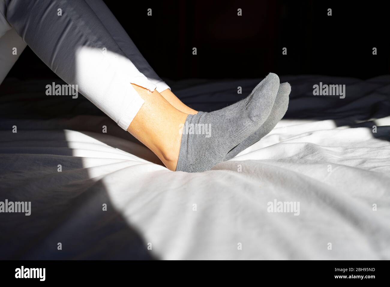 Feet in gray socks on the white bed in the morning. Stock Photo