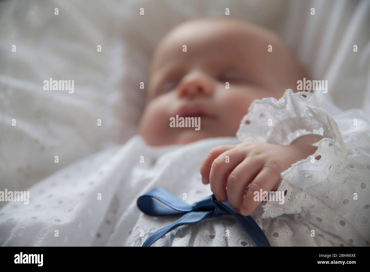 two months old baby with christening gown lying on white pillow Stock
