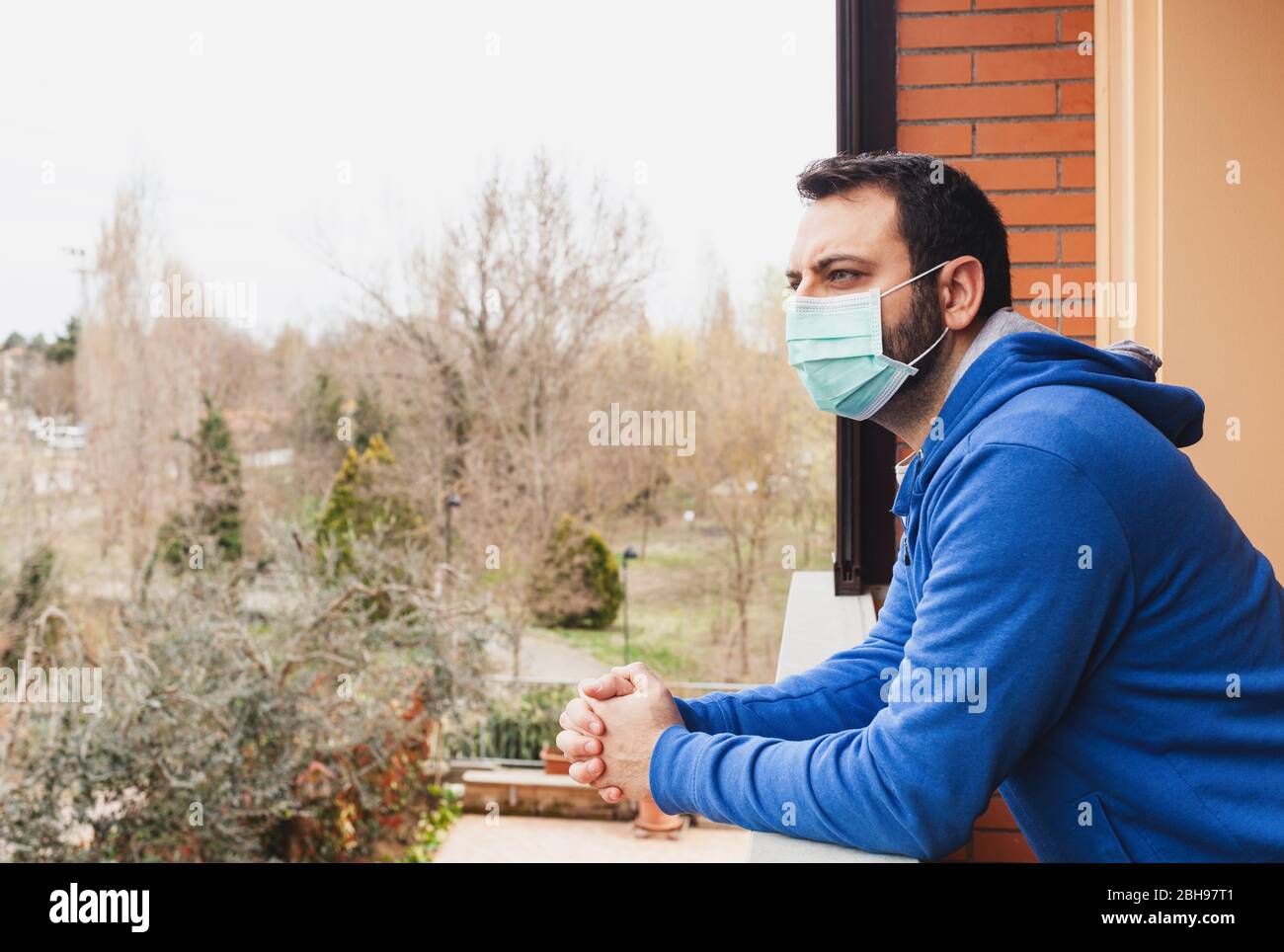 Young caucasian man with mask looking out onto home terrace during quarantine due to coronavirus covid19 pandemic. Stock Photo
