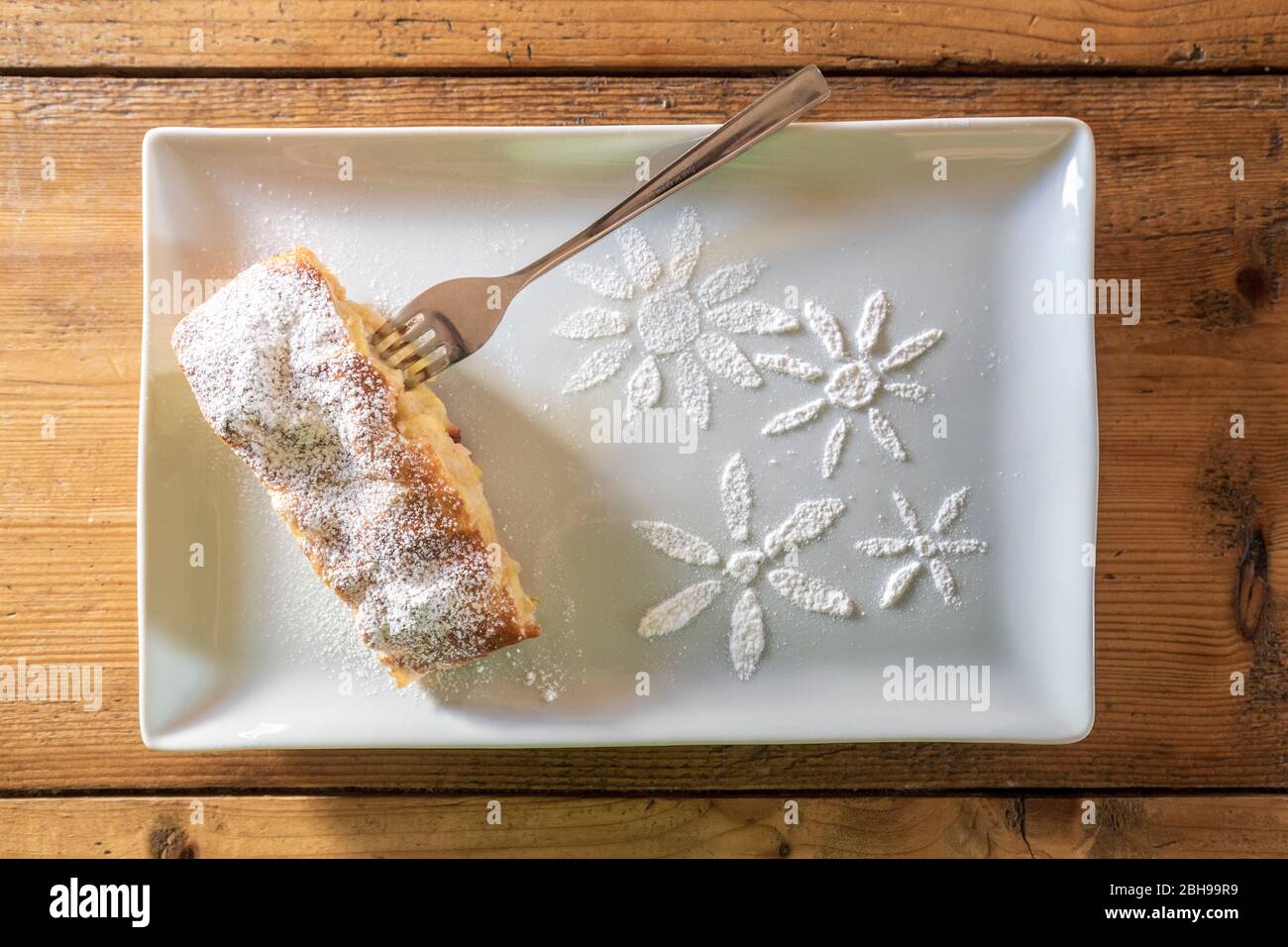 Delicious slice of apple strudel with powdered sugar and sugar decoration on a wooden table, typical dessert of the Dolomites and South Tyrol, Italy Stock Photo