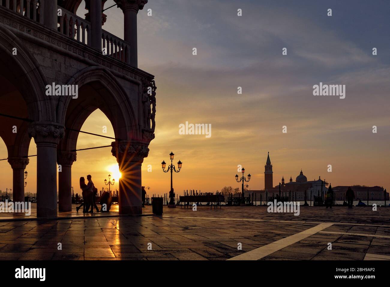 Doge's Palace on St. Mark's Square with romantic lovers in the backlight to the sunrise in the background San Giogio Maggiore and the Bacino di San Marco in between Stock Photo