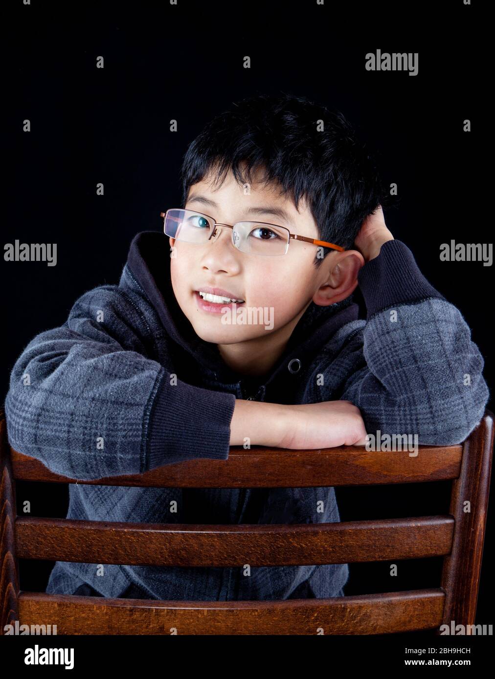 Handsome Asian Chinese boy posing in black hoodie sweater on the back of a chair in studio, isolated on black background. Stock Photo