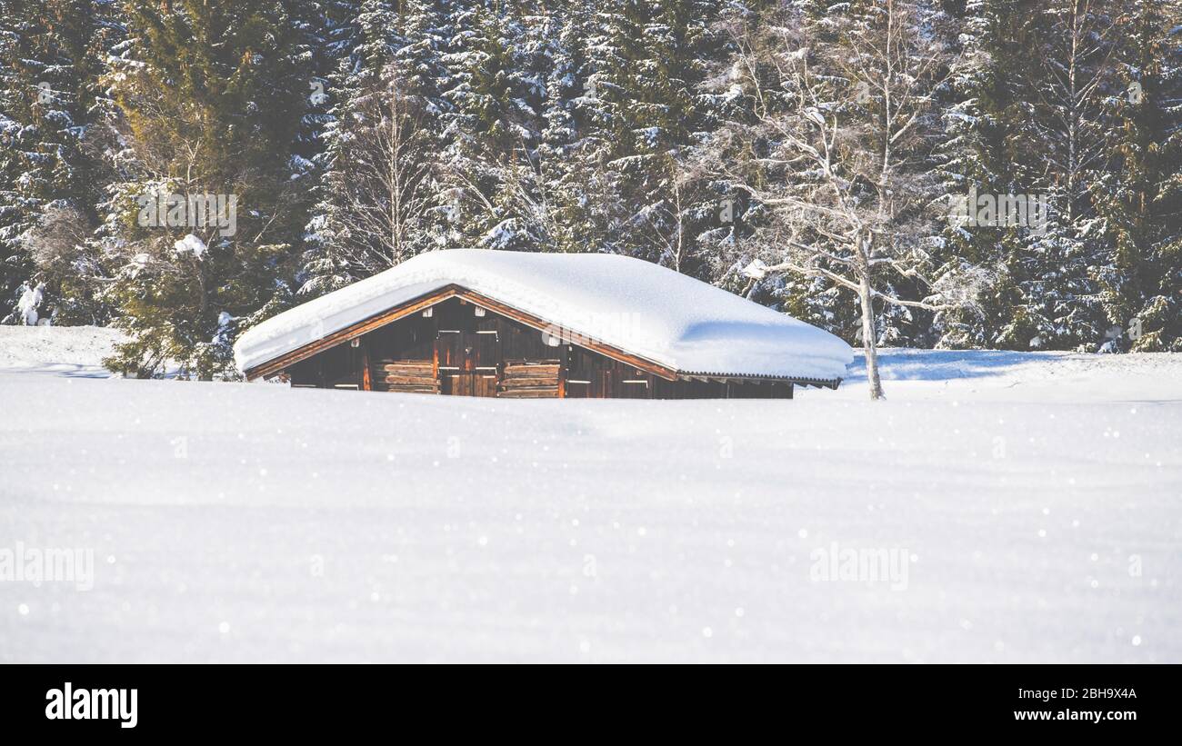 A snowy hut at Tennsee near Krün in winter with a view of the Wetterstein massif and the summits of the Alps at Landkreis Garmisch-Partenkirchen, Bavaria, Germany. Stock Photo