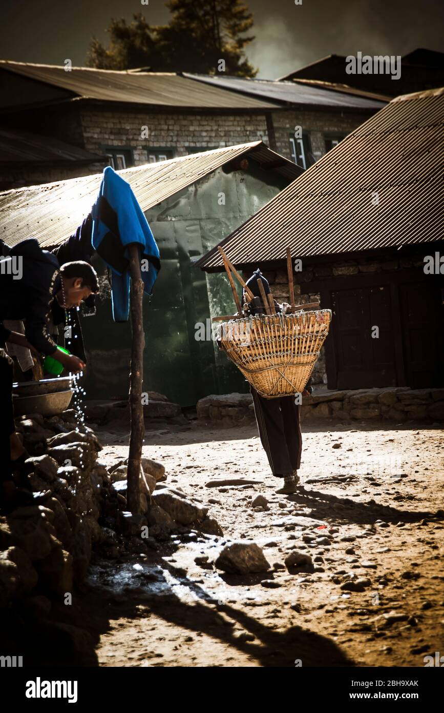Man with basket on his back runs through the village Stock Photo