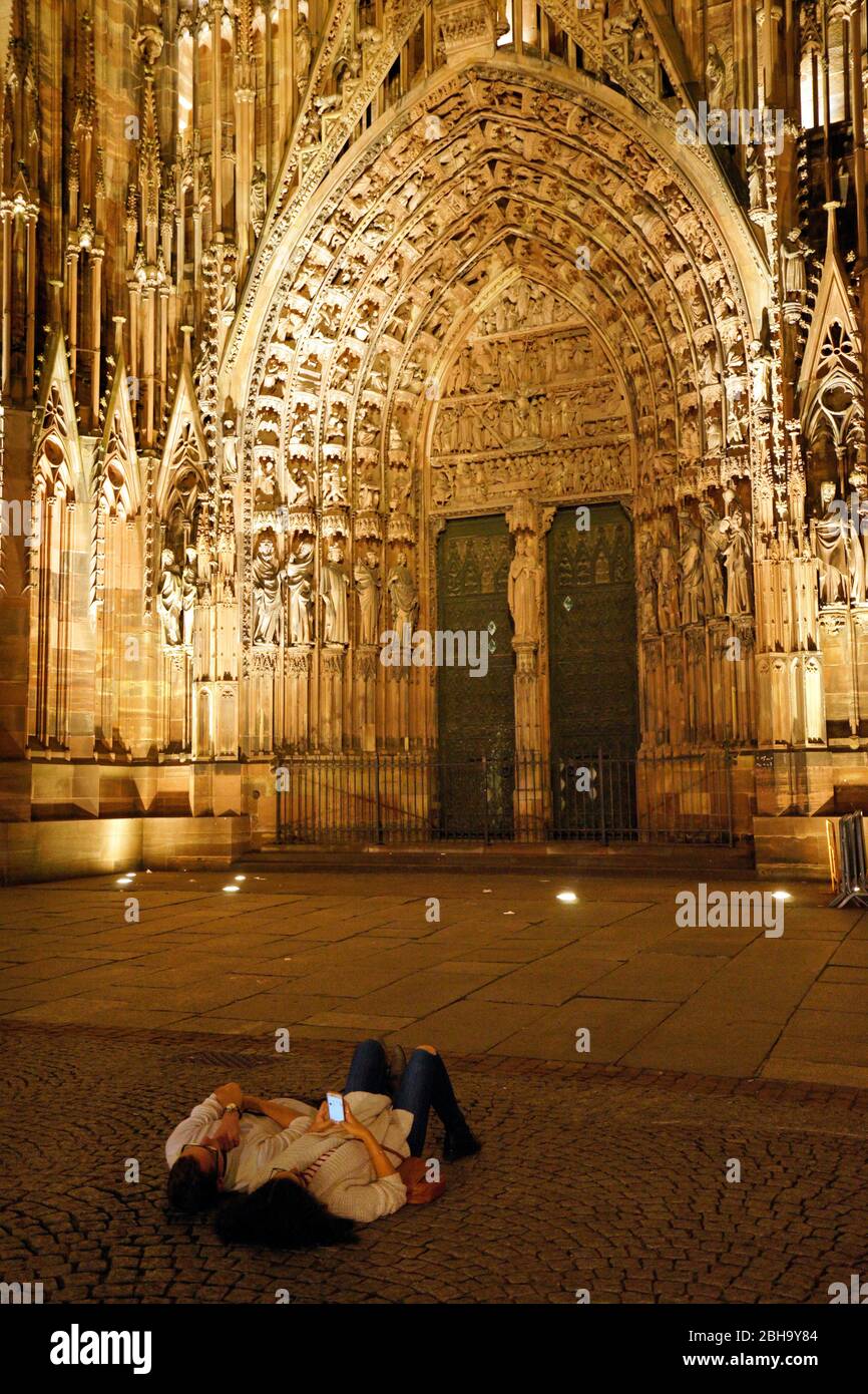 Frankreich, Elsass, Straßburg, Straßburger Münster, Westfassade, Hauptportal, abends, beleuchtet, zwei junge Leute liegen an einem warmen Sommerabend Stock Photo