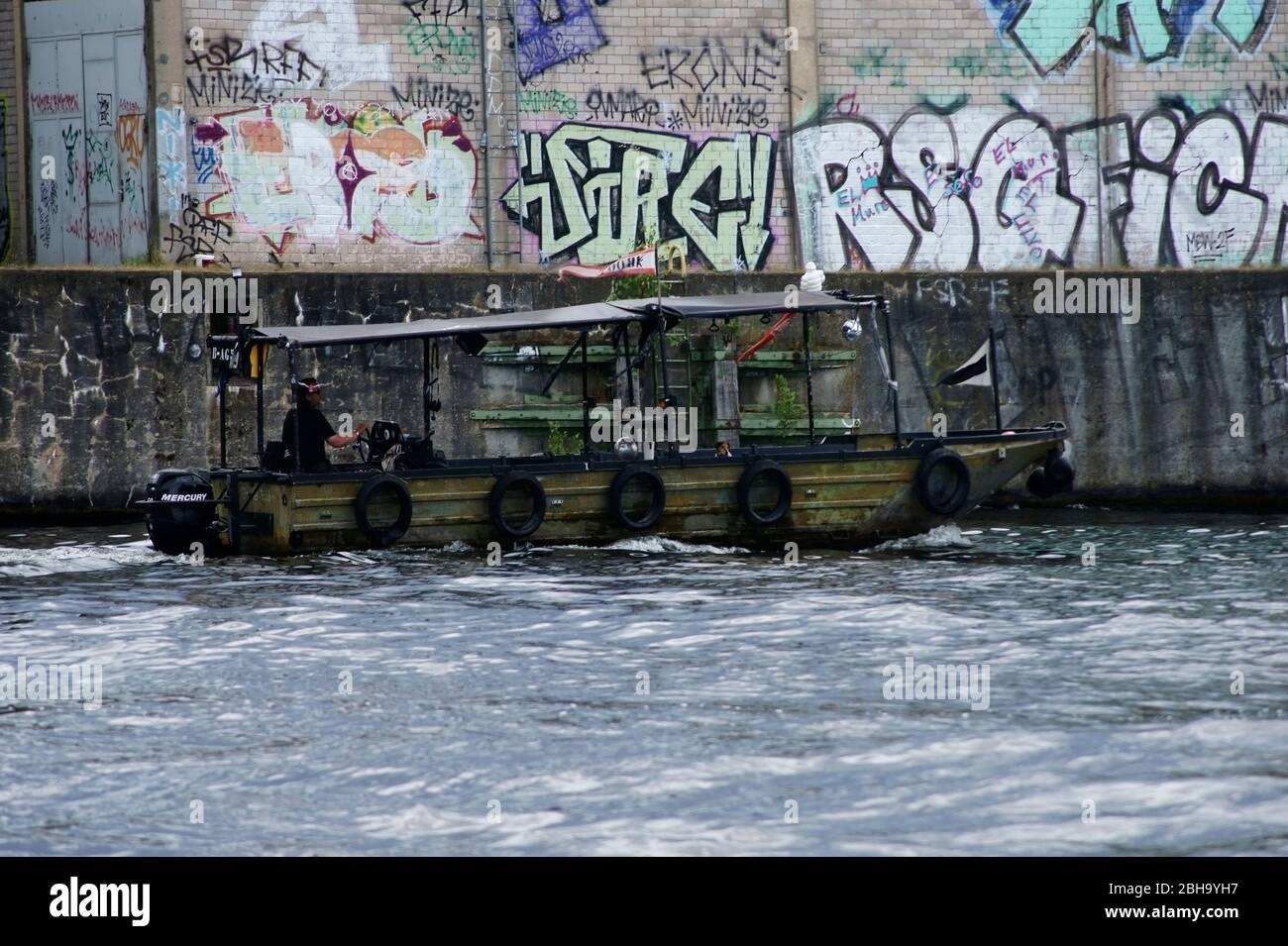 Berlin, Germany, a scrapped army patrol boat passes graffiti walls on the river Spree. Stock Photo