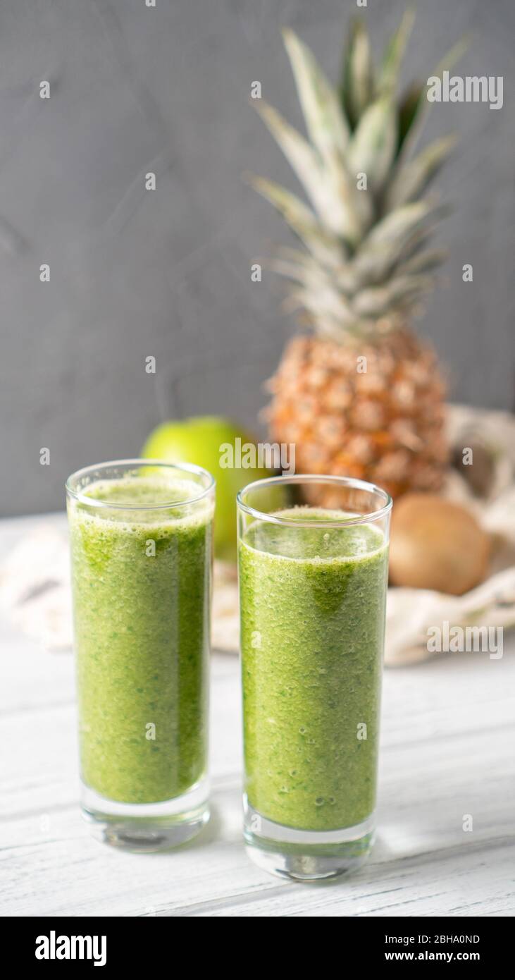 Apple pineapple kiwi smoothie on gray background with fruits behind. Refreshing green superpower summer drink. Vertical Stock Photo