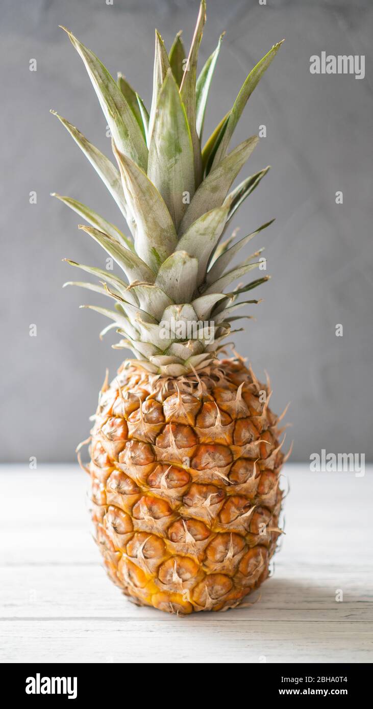 Single ripe illuminated pineapple on a white wooden table and gray background. Juicy standalone ananas. Stock Photo