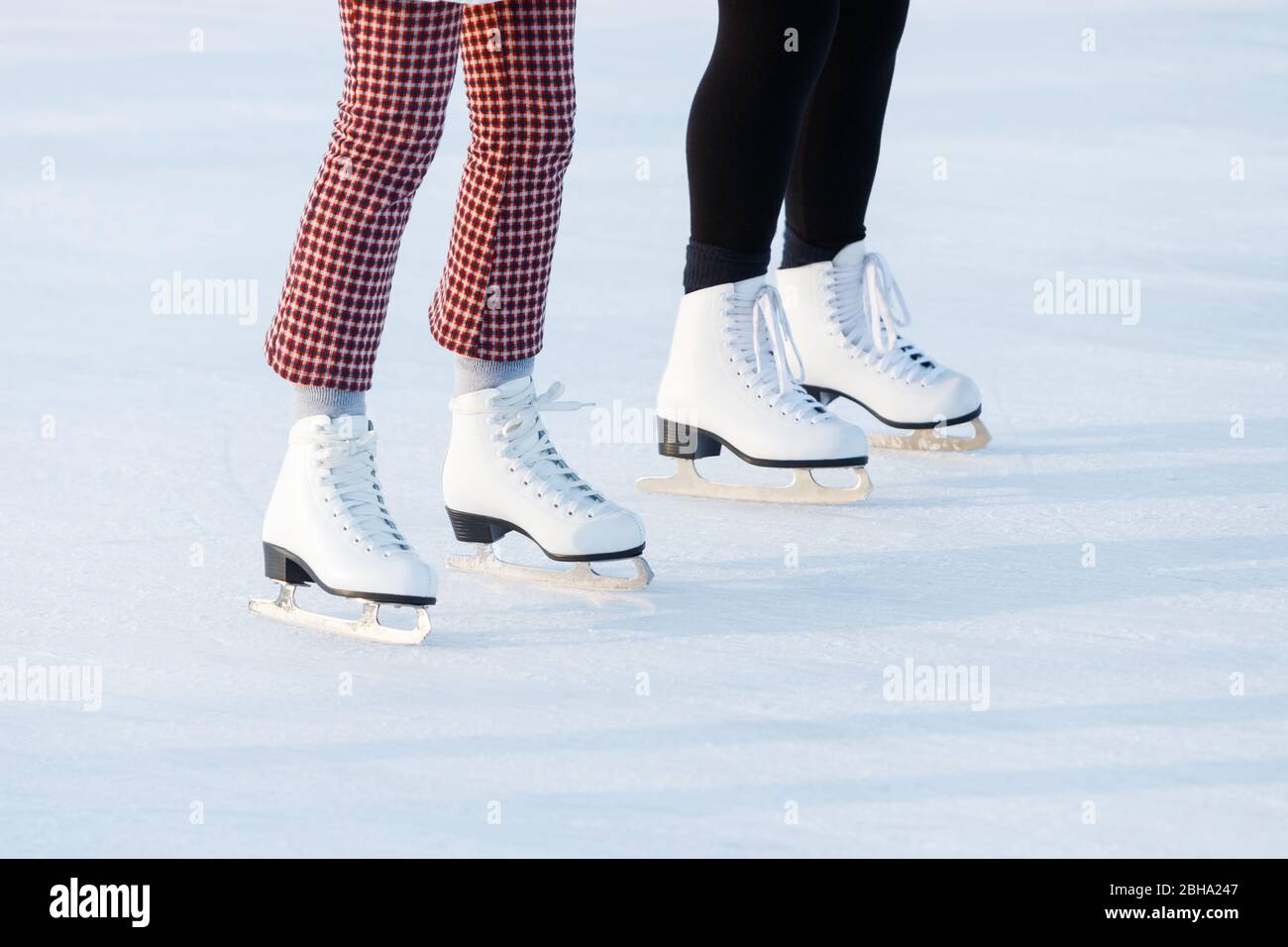 Close up of women's legs on skates in winter on an open skating rink. The ice skates of two friends skating together on a winter afternoon. Winter tim Stock Photo