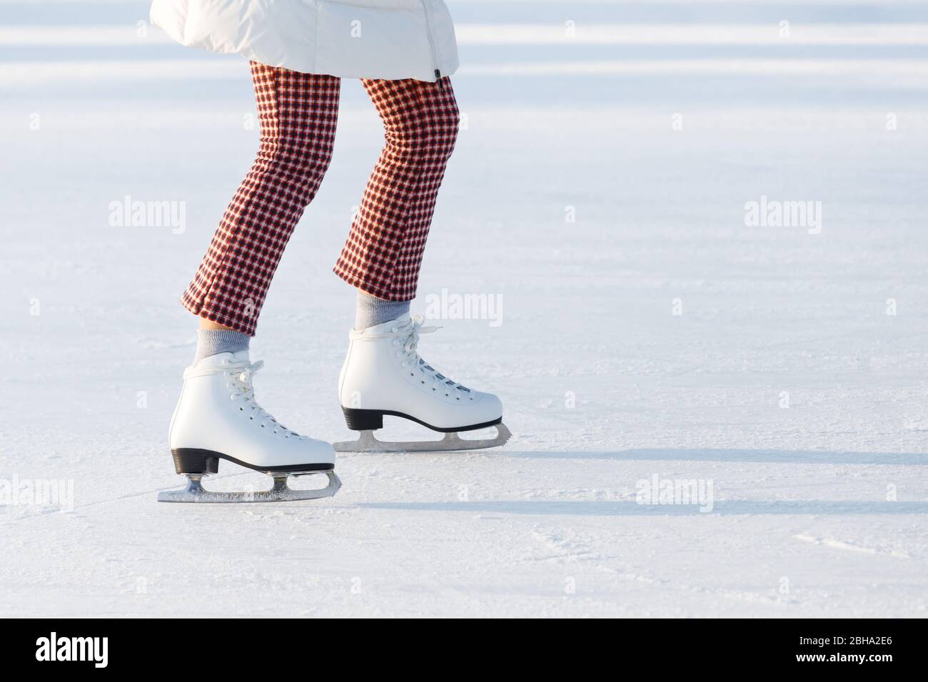 Close up of woman legs in red checked trousers on skates on an open skating rink, copy space. Sunny day. Winter sports in the city Stock Photo