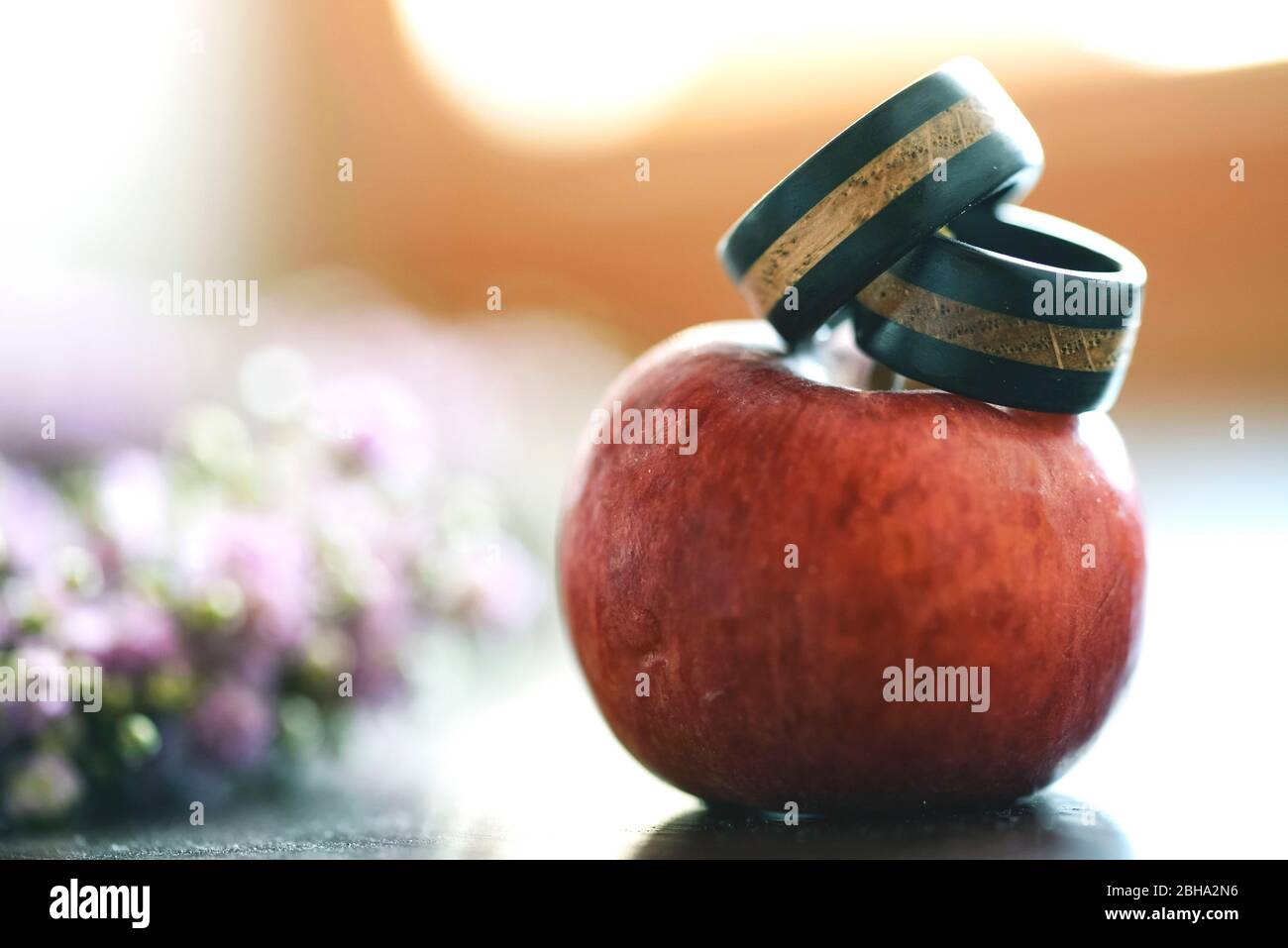 Wedding rings made of wood presented on an apple, closeup, floral arrangement, out of focus in the background Stock Photo
